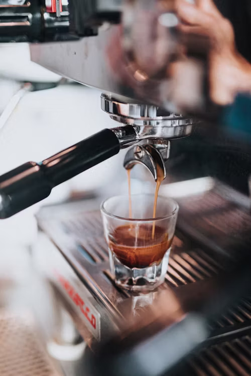 Barista mid-pour with visible steam rising, warm natural light, candid motion, cosy café background softly blurred